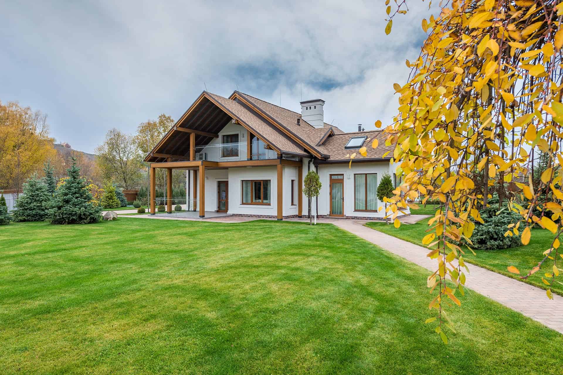 A modern house with a lush green lawn and a tree with autumn leaves, located in a residential area of Olathe, Kansas, showcasing the quality of artificial grass installations by Artificial Grass Olathe.